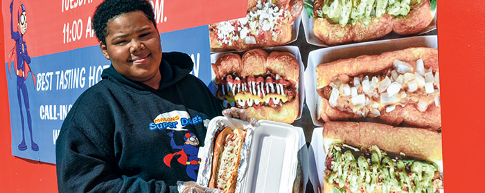 a boy holding a loaded hot dog in front of pictures of other hot dogs