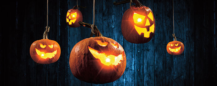 Lit pumpkins with carved faces in it hanging by ropes at the stems