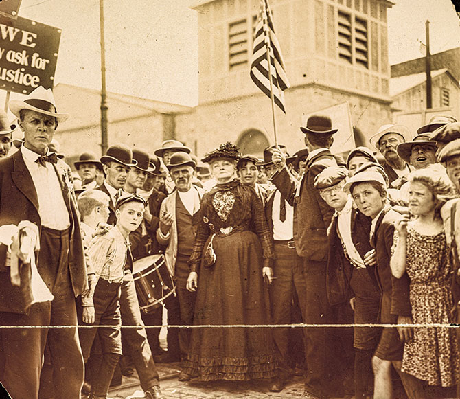 Black and white photo of a crowd of children looking forward as a woman stands in the middle of them