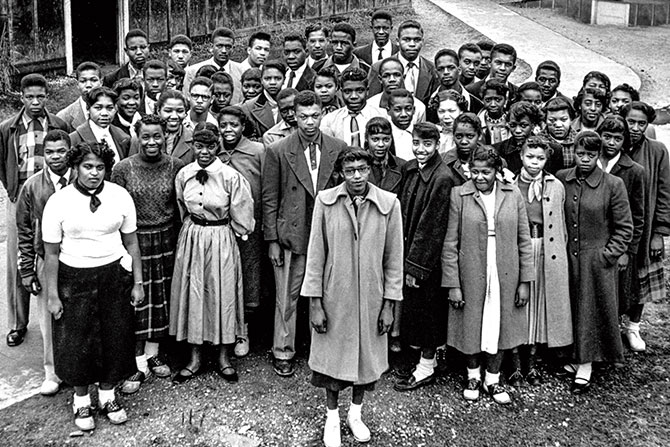 Black and white photo of a group of students with a single young woman in a long coat in the front