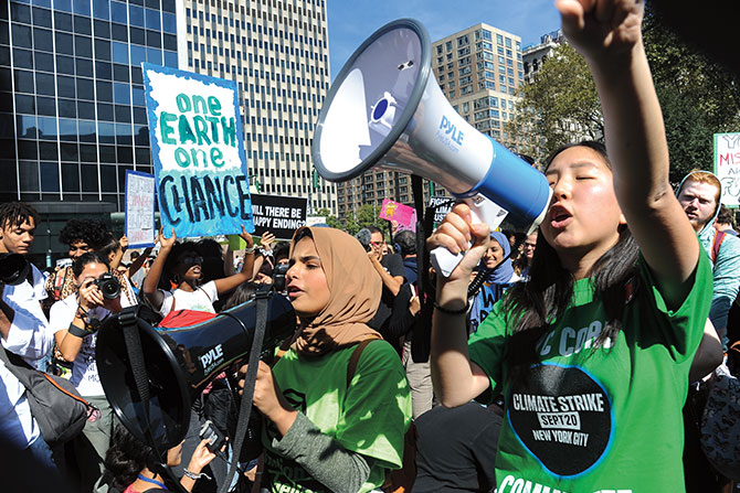Two young women with megaphones speaking to and wearing green shirts as people around them protest