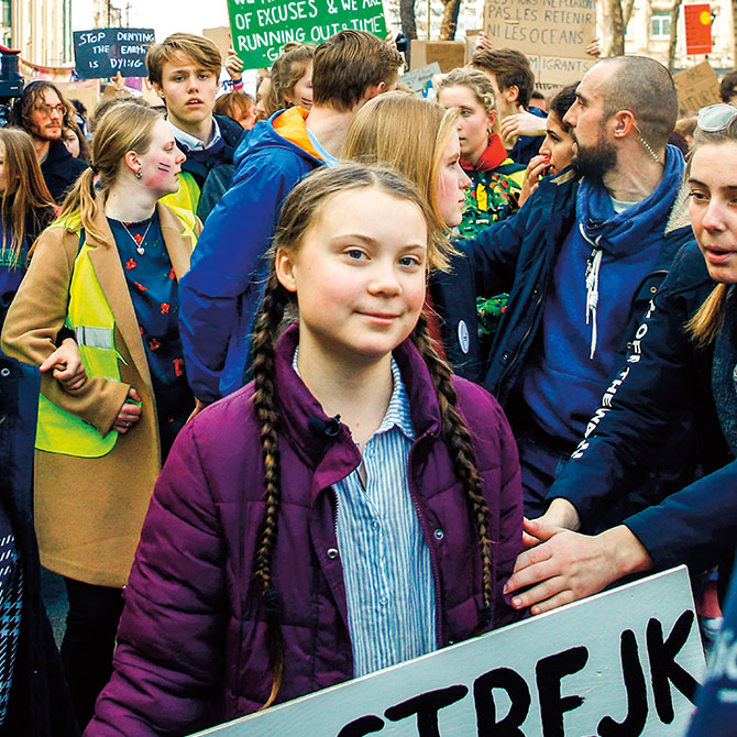 A young girl with long braided pigtails holding a sign as people protest to stop climate change