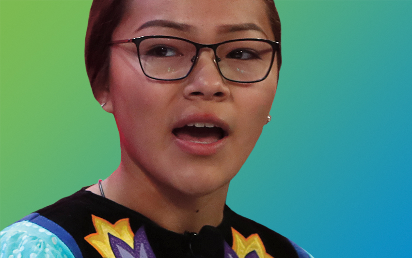 A young woman wearing glasses speaking into the podium microphone as she addresses an audience