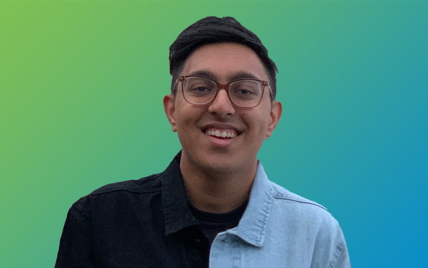 A smiling young man with brown glasses and a blue and black shirt