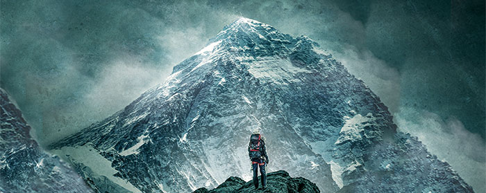 A man standing on a mountain looking at a much larger mountain in the distance