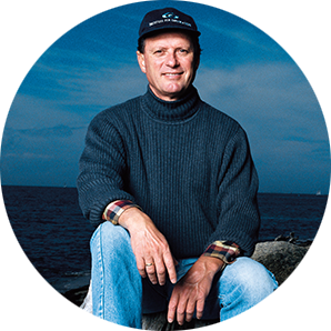 A smiling man with a cap on sitting down as he poses for a picture