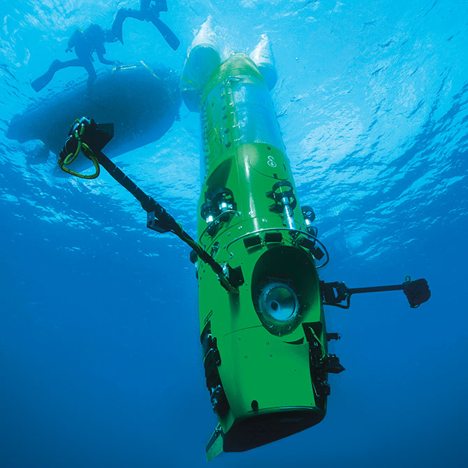 A long verticle yellow machine underwater as two divers swim above it next to their raft