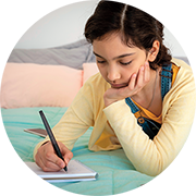 A girl writing on a notebook on her bed