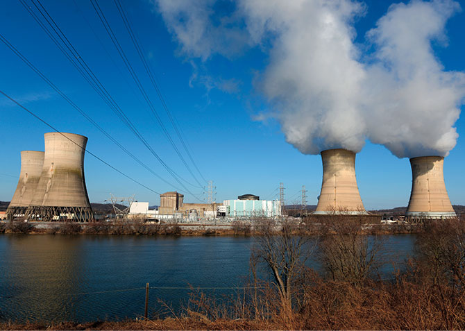 A nuclear power plant with smoke coming out of the tops of the large cone-like objects