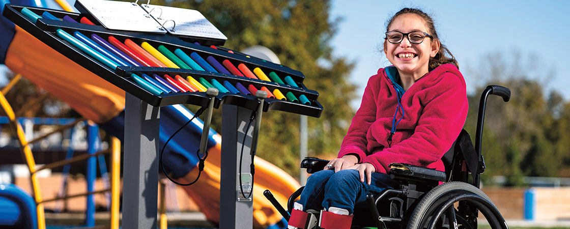 A smiling girl in a wheelchair sitting beside a xylophone