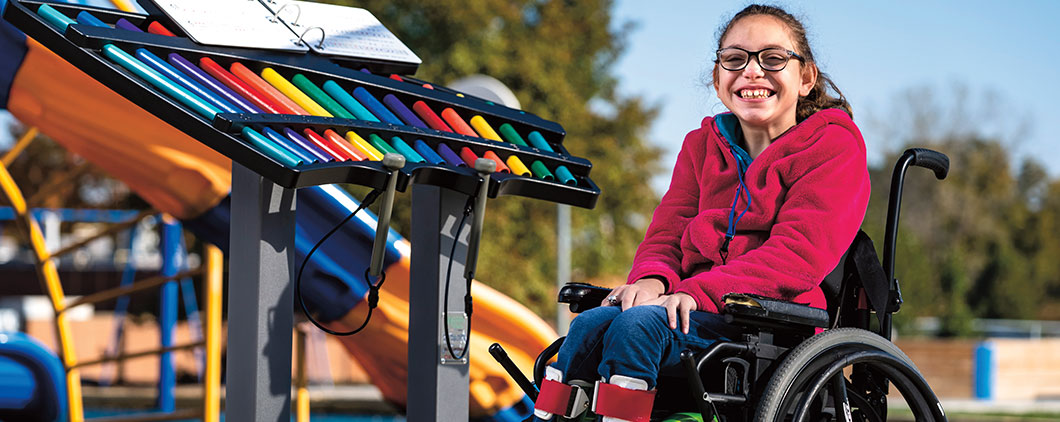 A smiling girl in a wheelchair sitting beside a xylophone