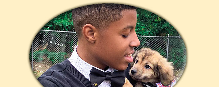 A boy holding a small dog. Both the boy and dog are wearing bow ties.