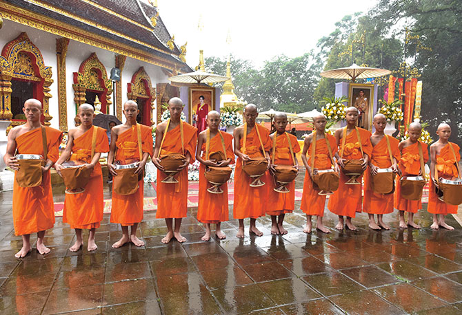 Boys in a place of worship dressed in orange monk robes with shaved heads and drums in their hands