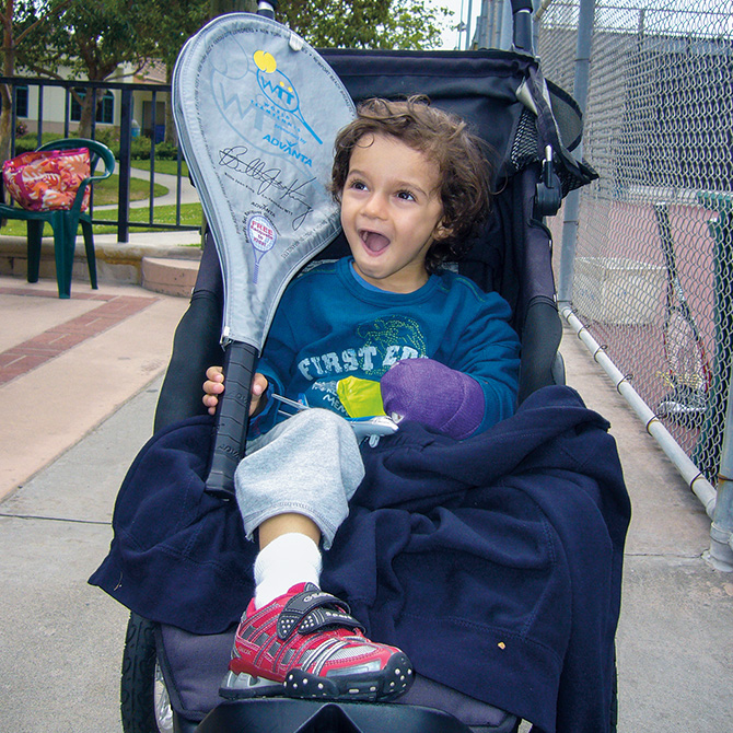 Photo of a toddler smiling with a tennis racket