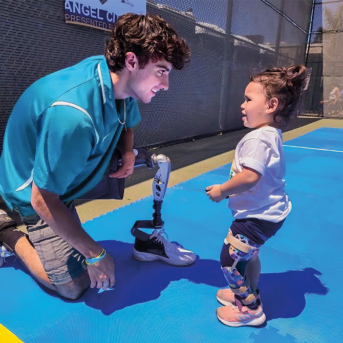 Photo of an athlete with a prosthetic leg talking to a toddler with a prosthetic leg