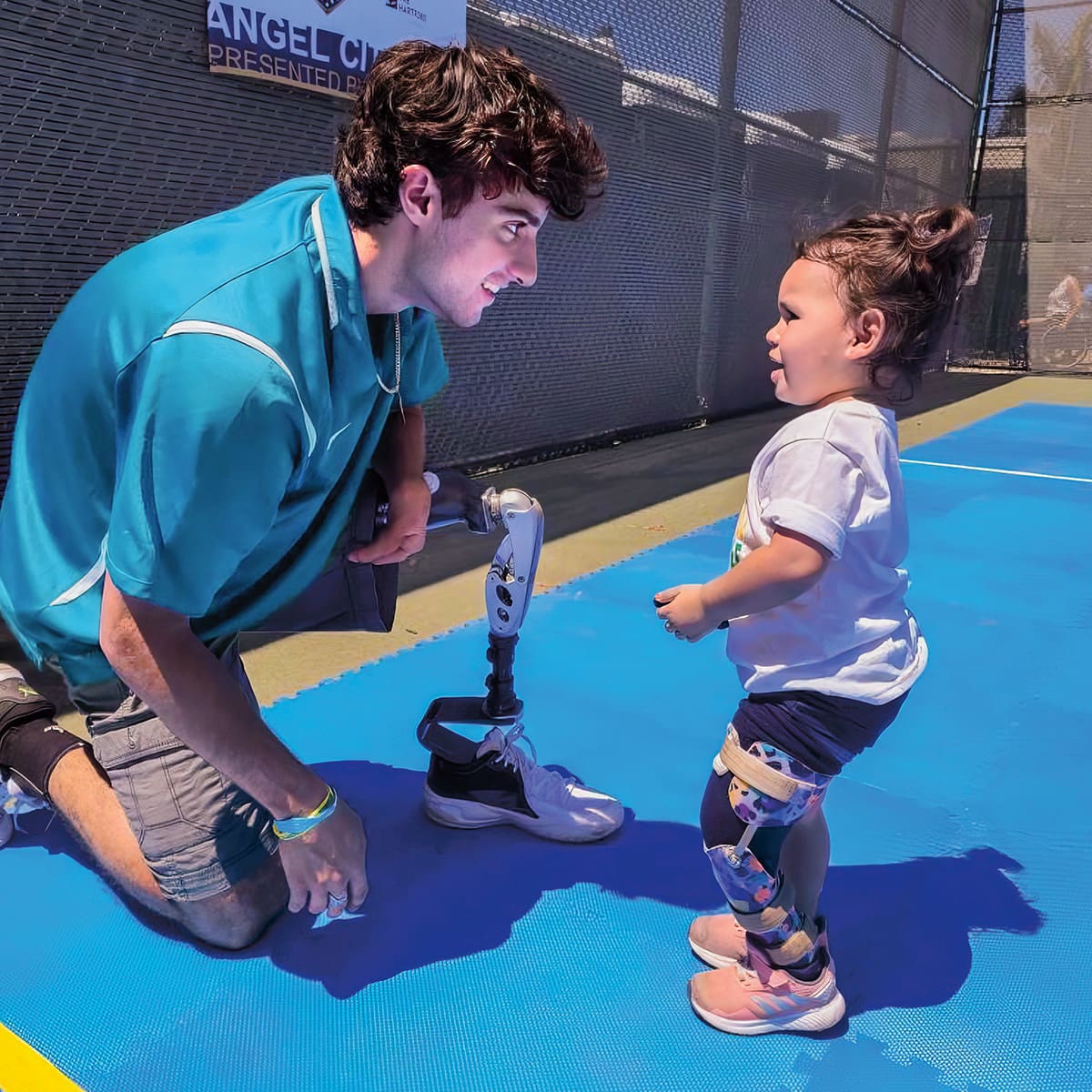 Photo of an athlete with a prosthetic leg talking to a toddler with a prosthetic leg