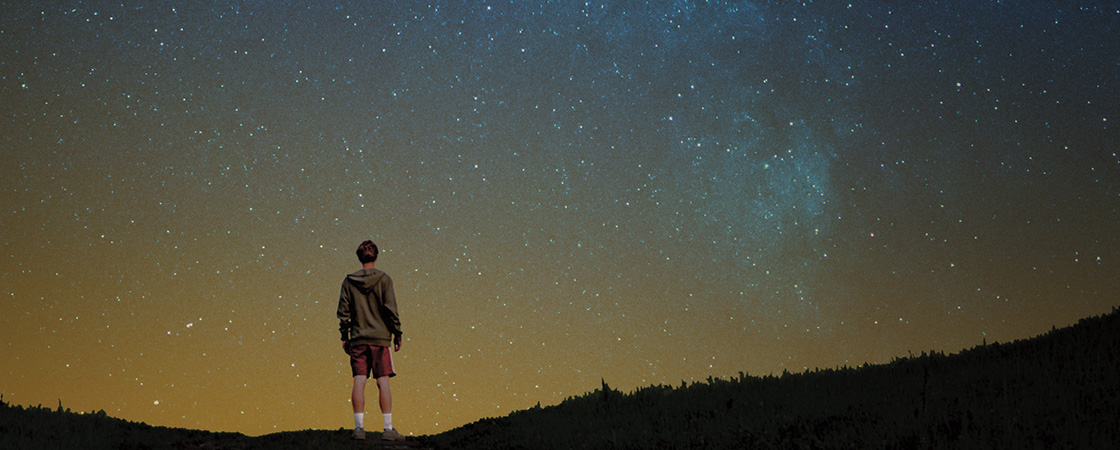 Person standing in a field alone looking up at the night sky full of stars