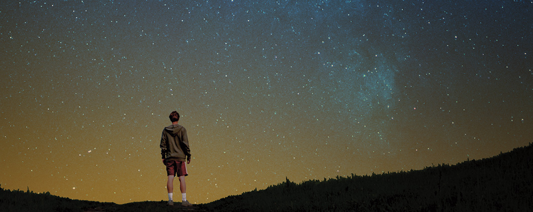 Person standing in a field alone looking up at the night sky full of stars