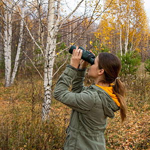 A woman looking up into the trees with binoculars